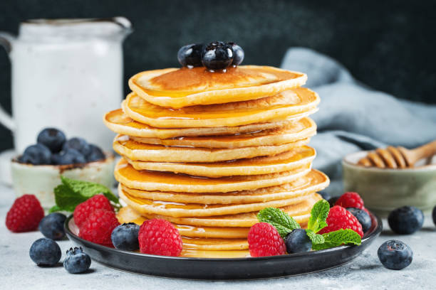 istock Delicious pancakes, with fresh blueberries, raspberry and maple syrup or honey on a dark background 1461214970
