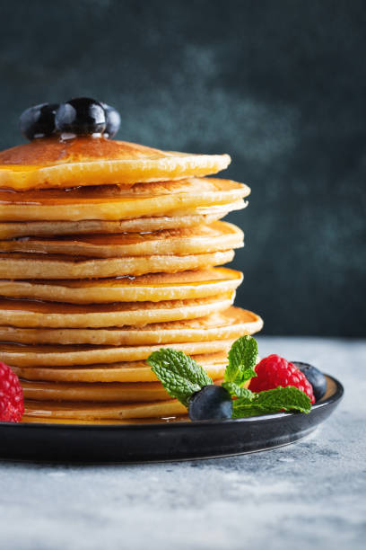 istock Delicious pancakes, with fresh blueberries, raspberry and maple syrup or honey on a dark background 1461214977