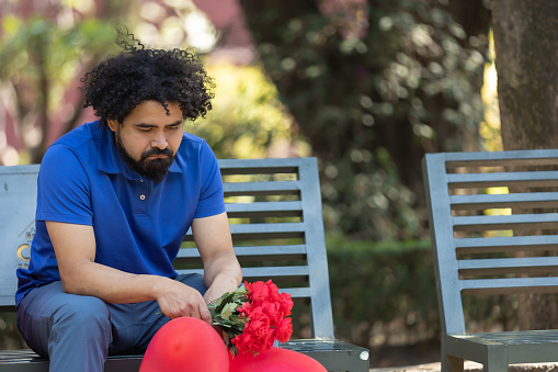 Sad Mexican man sitting on park bench on valentine day, bad date