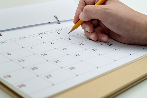 Woman hand with pencil writing on calendar page.