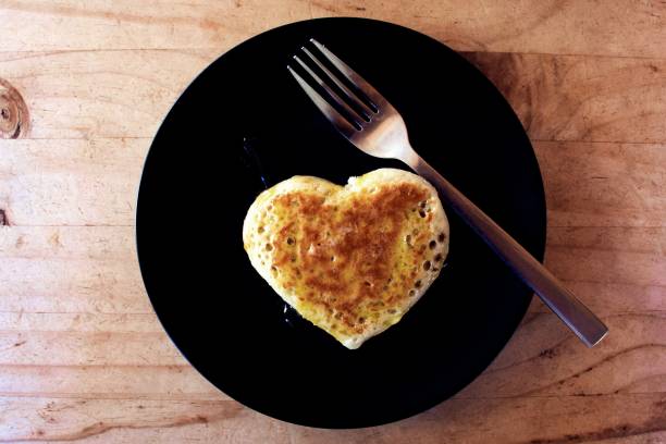 A background of a homemade love heart shaped crumpet for breakfast on a plate with a fork.