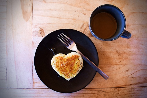 A background of a homemade love heart shaped crumpet for breakfast on a plate with a fork.