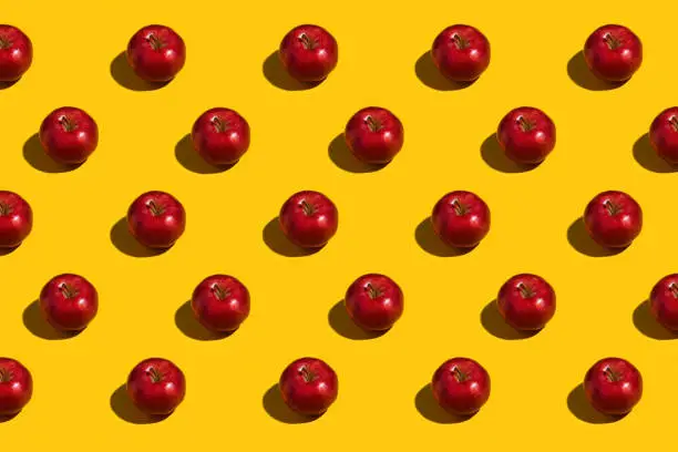 Overhead view of rows of shiny red apples on a bright yellow background