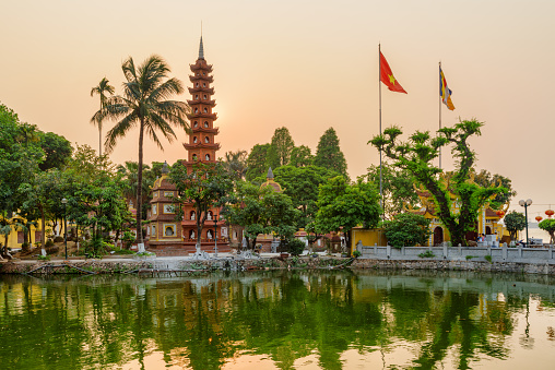 Hanoi, Vietnam - April 19, 2019: Fabulous sunset view of the Tran Quoc Pagoda and West Lake. The flag of Vietnam (red flag with a gold star) and the Vietnamese Buddhist flag fluttering over the lake.