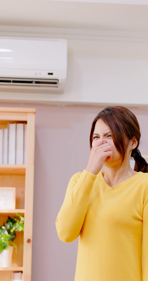 asian woman feel annoyed and she is suffering bad smell from heating or ac at home - trying clinch nose holding breath