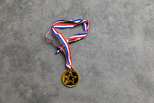 A closeup of a hand holding the first place gold trophy medal isolated on pale greenish background.