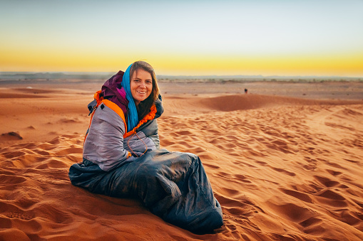 Woman tourist enjoying time before sunrise sitting on sand dunes in the desert, Merzouga, Erg Chebbi sand dunes region, Sahara, Morocco.