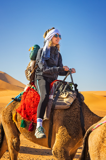 Woman tourist riding camels on sand dunes in the desert, Merzouga, Erg Chebbi sand dunes region, Sahara, Morocco. Model released.