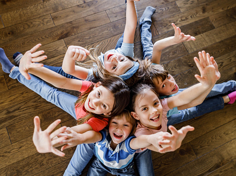 High angle view of group of happy little friends sitting back to back with raised arms and looking at camera.