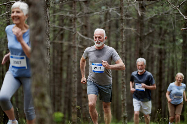 Happy active seniors enjoying while running a marathon race through forest. Focus is on man.