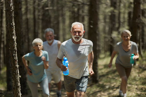Determined mature man and his friends running a sports race through the forest.