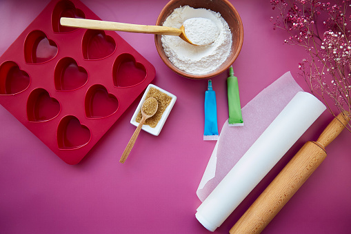 Preparing for baking: heart-shaped silicone mold, rolling pin, confectionery syringe, glaze, flour, sugar on pink background. Valentine's day concept. High quality photo