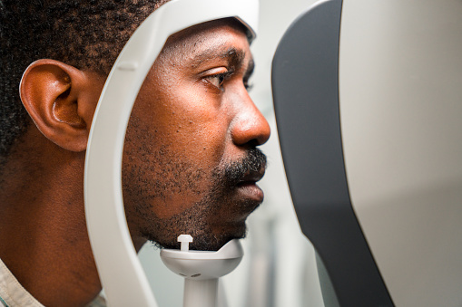 Side view of male bearded patient looking straight into optometry screen. He is focused and serious.