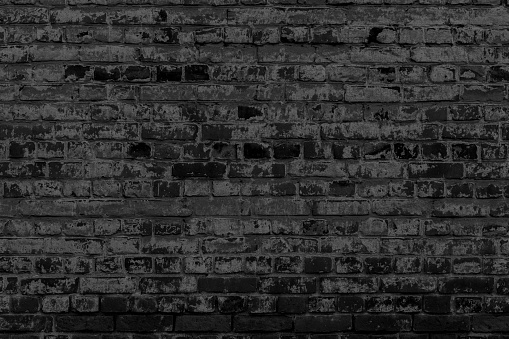 Old black brick wall. Peeling white paint on a black wall.
