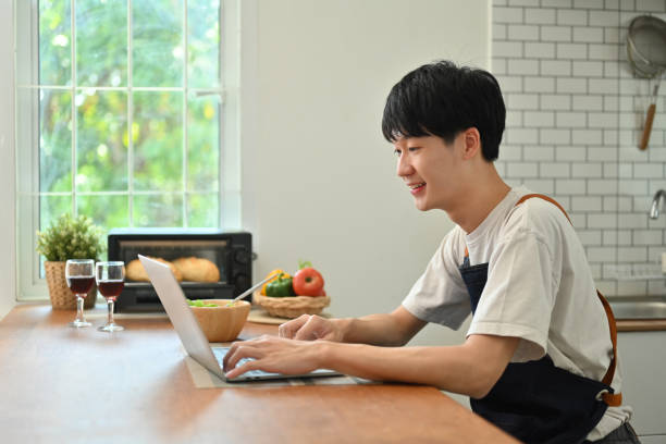 istock Side view of handsome man using laptop while sitting in modern sunny kitchen, Freelancer working remote from home. 1461270297