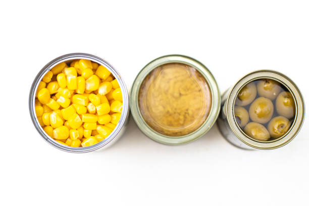 Top view of tin with tuna placed between cans with corn and olives on white background