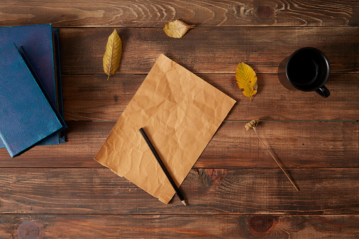Pencil and blank paper wooden background with cup of coffee, book and autumn leaves.