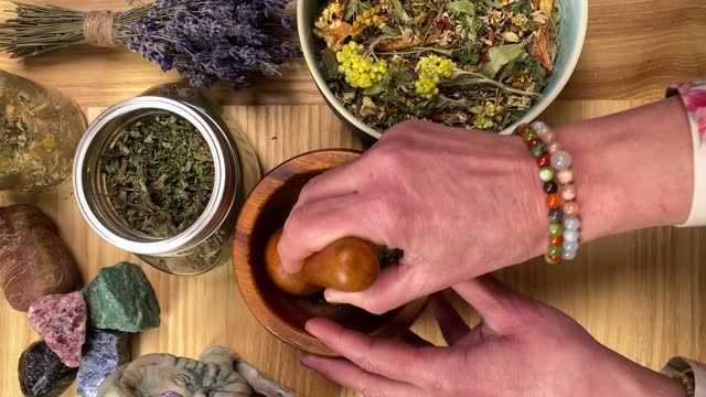 Table top view herbalist mixing dried herbs with mortar pestle indoors