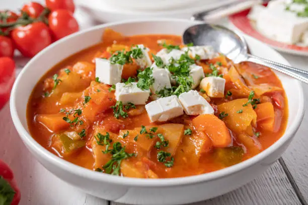 Delicious cabbage soup or stew with mediterranean vegetables such as tomatoes, carrots, zucchini, onions, garlic, herbs and bell peppers. Served with cubed feta cheese on a plate. Closeup and front view