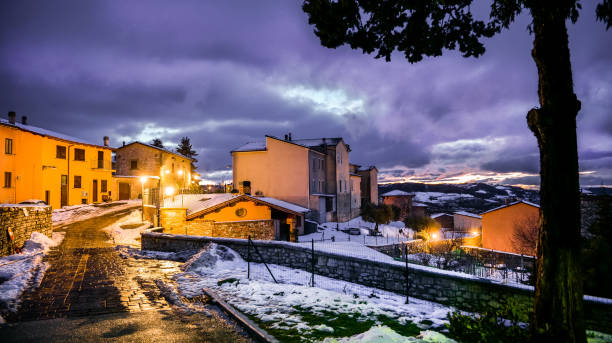 A winter atmosphere at twilight in the snowy alleys of a medieval village in Umbria A winter atmosphere at twilight in the snowy alleys of the medieval village of Gualdo Tadino in Umbria, central Italy. The Umbria region, considered the green lung of Italy for its wooded mountains, is characterized by a perfect integration between nature and the presence of man, in a context of environmental sustainability and healthy life. In addition to its immense artistic and historical heritage, Umbria is famous for its food and wine production and for the high quality of the olive oil produced in these lands. Image in 16:9 ratio and high definition quality. gualdo tadino stock pictures, royalty-free photos & images