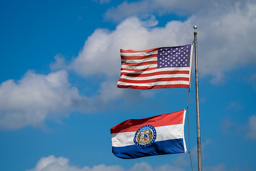 The national flags of America and Missouri on the pole waving in the wind against a cloudy sky