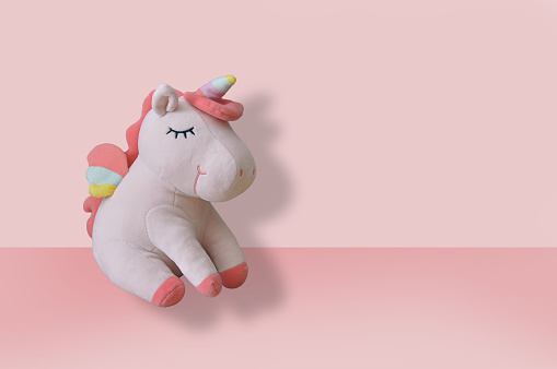 Cute soft unicorn plush toy on pink background. Close up shot, empty space