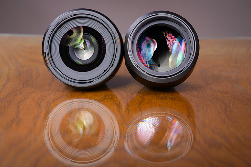 Two camera lenses with colorful light reflections on a wooden table