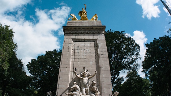 A low-angle of a statue in Columbus Circle and Central Park, trees and cloudy sky background