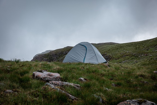 A tent on top of the big green mountain under the gray gloomy cloudy sky