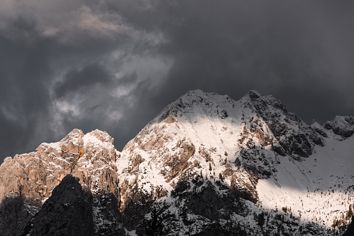 A closeup of a peak of mountain chain covered with snow and sunlight against the cloudy sky