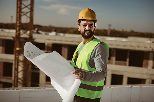 Portrait of professional engineer with safety helmet holding a blue print and looking away