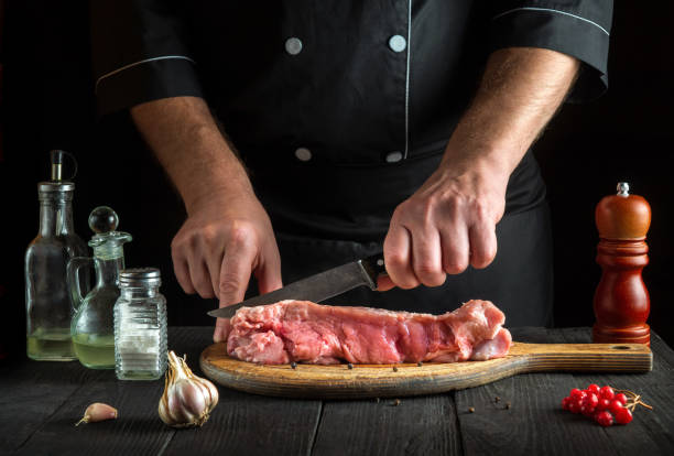 istock Professional chef cuts meat with a knife before baking. Spices on kitchen table in a restaurant for preparing a delicious lunch. 1461302377