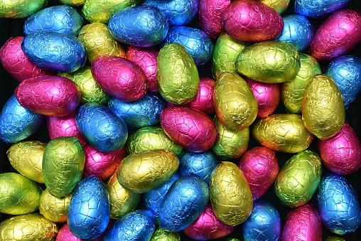 Pile or group of multi colored colourful foil wrapped chocolate easter eggs in pink, blue, yellow and lime green.