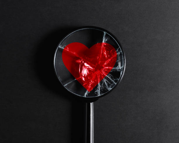 Concept of broken heart, destroyed love and relationships, cardiovascular disease. Broken magnifier focused on red heart icon on black background stock photo
