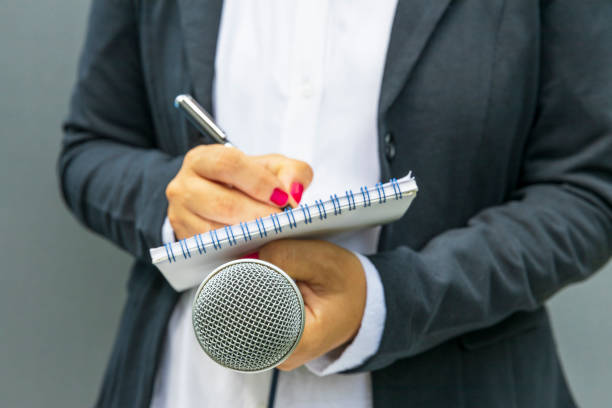istock Female journalist at news conference, writing notes, holding microphone 1461311646