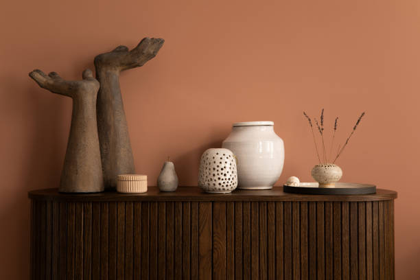 istock Interior design of harmonized living room interior with wooden commode, modern hands sculpture, vase with dried flowers, beige casket, pink wall and personal accessories. Home decor. Template. 1461313312