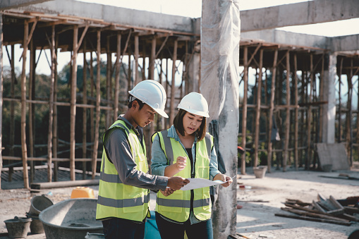 Two specialists inspect commercial, Industrial building construction site. Real estate project with civil engineer, designing commercial buildings on paper. Skyscraper concrete formwork frames.