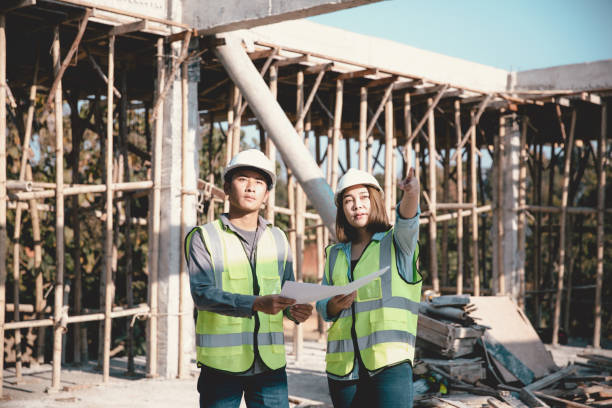 istock Two specialists inspect commercial, Industrial building construction site. Real estate project with civil engineer, designing commercial buildings on paper. Skyscraper concrete formwork frames. 1461313629