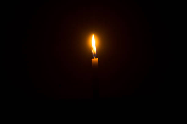 istock Single burning candle flame or light glowing on an orange candle on black or dark background on table in church for Christmas, funeral or memorial service 1461316839
