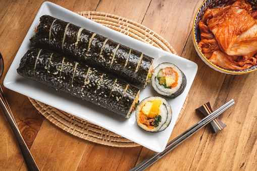 Korean Sushi Rolls or Kimbap is a popular Korean dish in white plate on wooden table, California Maki,  Steamed rice wrapped in seaweed with shrimp eggs meat and vegetable.