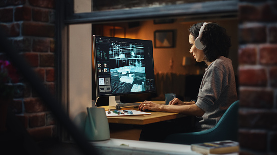 Creative Female 3D Architect Artist Using Desktop Computer with Display Showing CAD Real Estate Project. Brazilian Woman Video Game Developer Creating Gaming Level. View Into the Apartment Window.