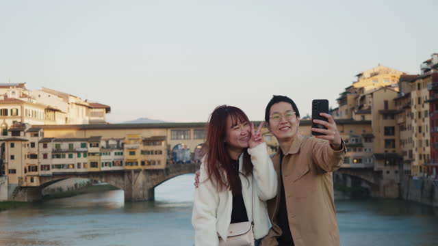 An asian couple is taking a selfie in Florence, Italy, with Old Bridge in the background
