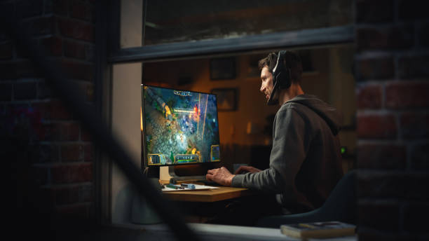 istock Focused Middle Aged Male Gamer Playing Online Video Game on Personal Computer. Guy Enjoying Fantasy RPG Game with Role Playing Character Casting Spells, Destroy Enemies. Shot from Outdoors. 1461320515
