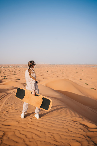 Woman with sandboard standing in the dunes.  Popular tourist attraction in Dubai desert