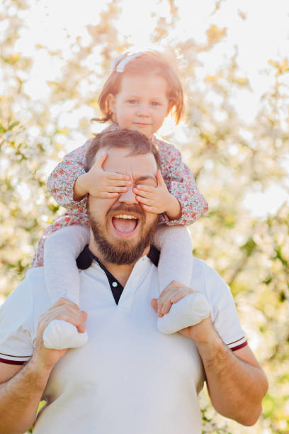 istock in sun's rays. Dad plays and rolls on shoulders his daughter in spring garden. 1461322346