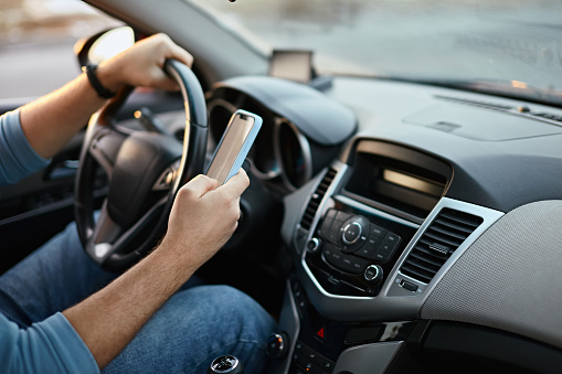 Hands of unrecognizable man driver using mobile phone while driving.