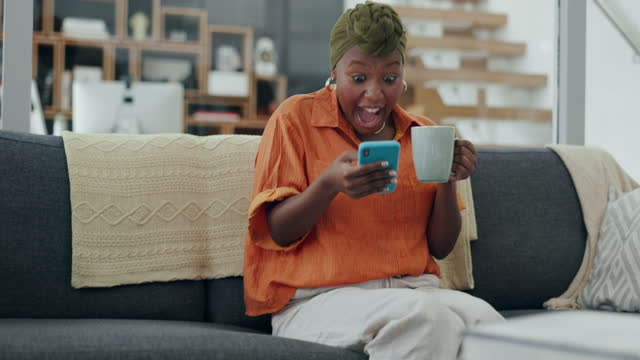 Excited, celebration and black woman with phone on sofa, smile from good news, success and victory. Technology, happiness and girl with coffee at home celebrating bonus and winning online competition