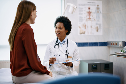 African American doctor and her female patient communicating during examination at medical clinic.