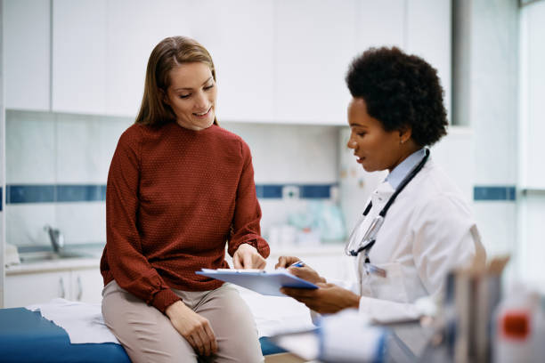 mujer feliz revisando sus datos médicos con una doctora negra en la clínica. - physical checkup fotografías e imágenes de stock