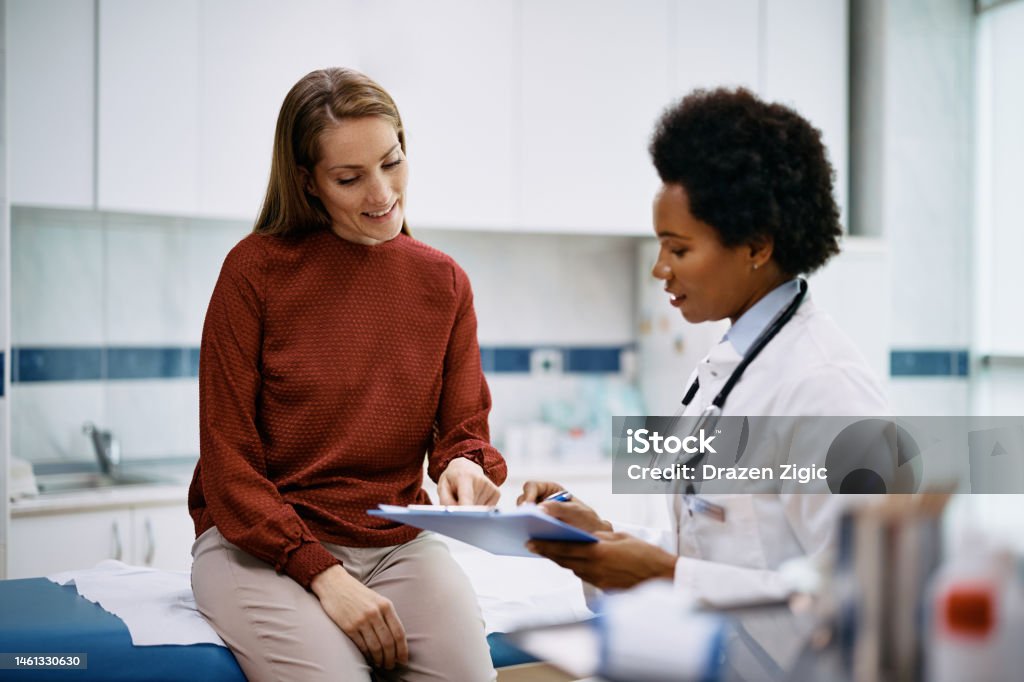 Happy woman going through her medical data with black female doctor at the clinic. African American doctor and her female patient analyzing medical report after examination in the hospital. Focus is on female patient. Doctor Stock Photo